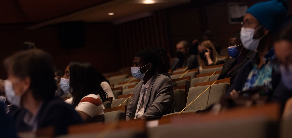 Hombres y mujeres sentados en un auditorio usando tapabocas.