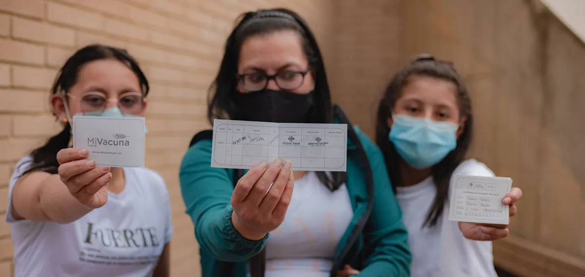 Mamá con sus dos hijas mostrando el carné de vacunación