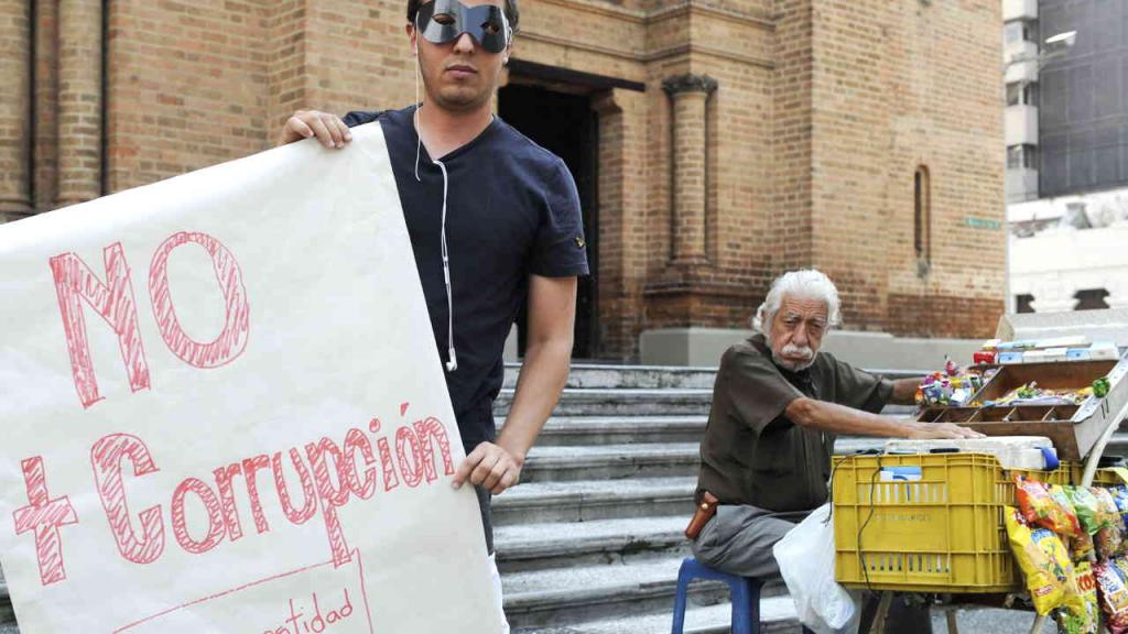 Un hombre que usa un antifaz sostiene un cartel en el que se lee no más corrupción.