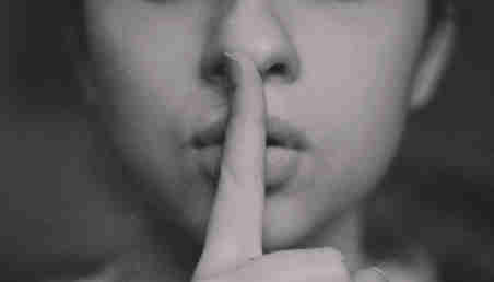 Una mujer pone un dedo en sus labios, señalando con su gesto que guarda silencio. 
