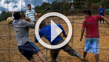 Hombres jugando fútbol. La escena se ve a través de la red de una cancha. 