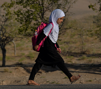 Niña afgana camina con una mochila en la espalda.