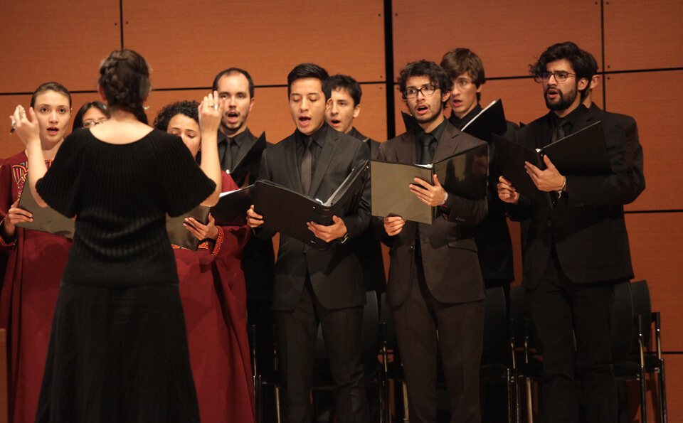un coro de hombres de negro y mujeres con vestido vinotinto interpreta un himno