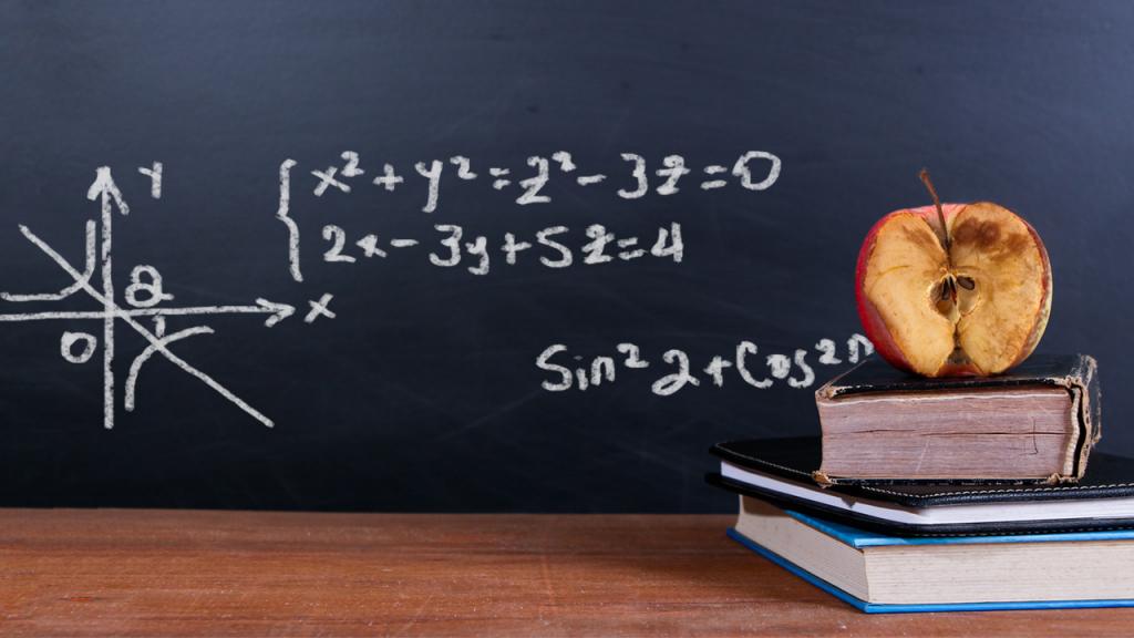 Una manzana podrida sobre dos libros frente a un tablero con signos matemáticos. 
