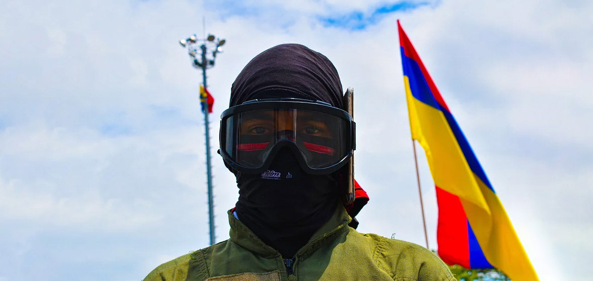 Hombre con capucha en primer plano. Atrás la bandera de Colombia.