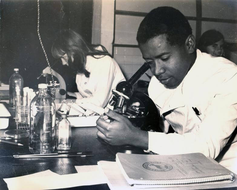 estudiantes en laboratorio mirando por un microscopio. La foto es antigua y en blanco y negro