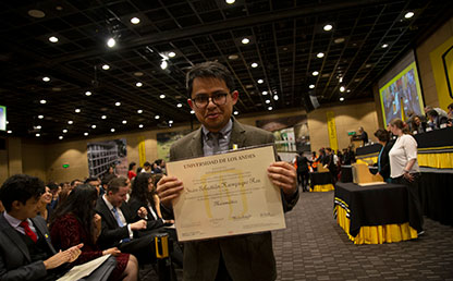 Hombre joven sostiene su diploma de grado a media altura y sonríe para la foto.