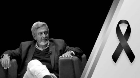 Guillermo Perry, economista colombiano sentado en una silla. A un lado de la imagen una cinta negra por su fallecimiento. 