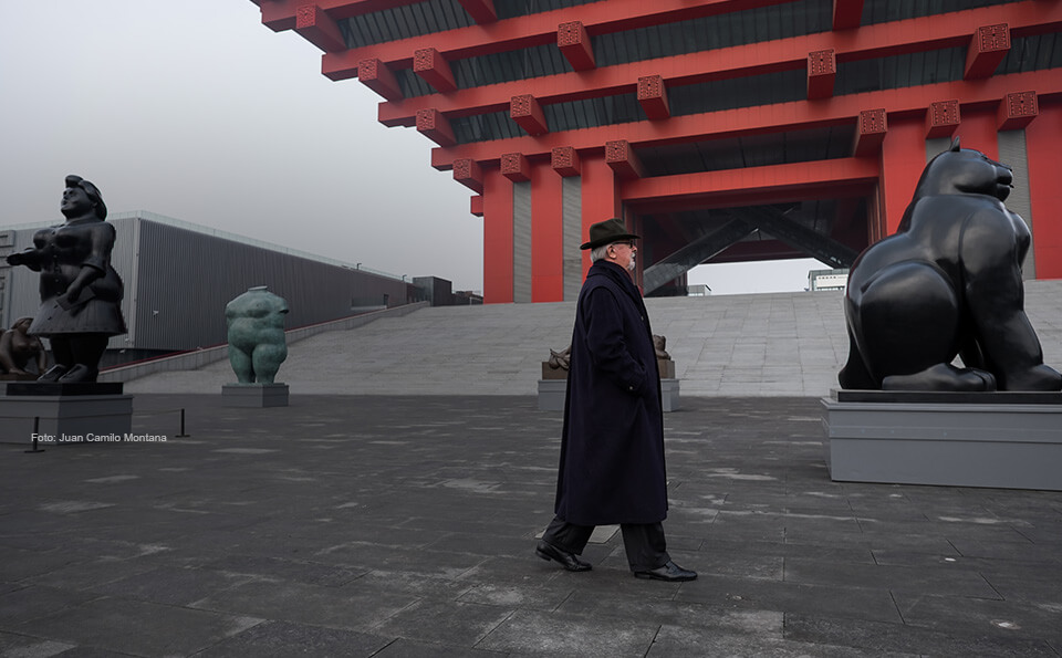 hombre mayor con gabán camina por unas obras de Botero en China