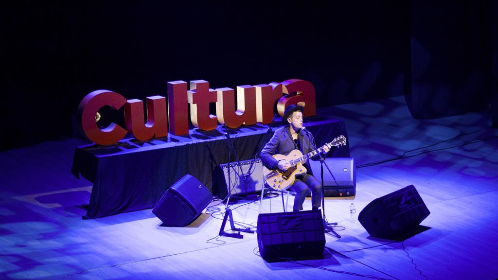 Hombre tocando la guitarra, atrás un aviso con la palabra cultura.