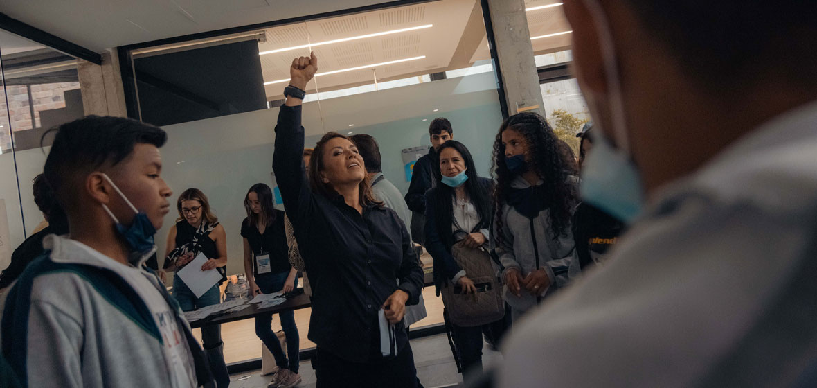 Una mujer alza el brazo frente a un grupo de estudiantes. 