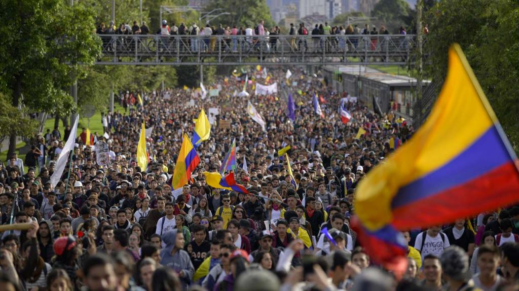 Personas marchando y a un lado la bandera de Colombia.