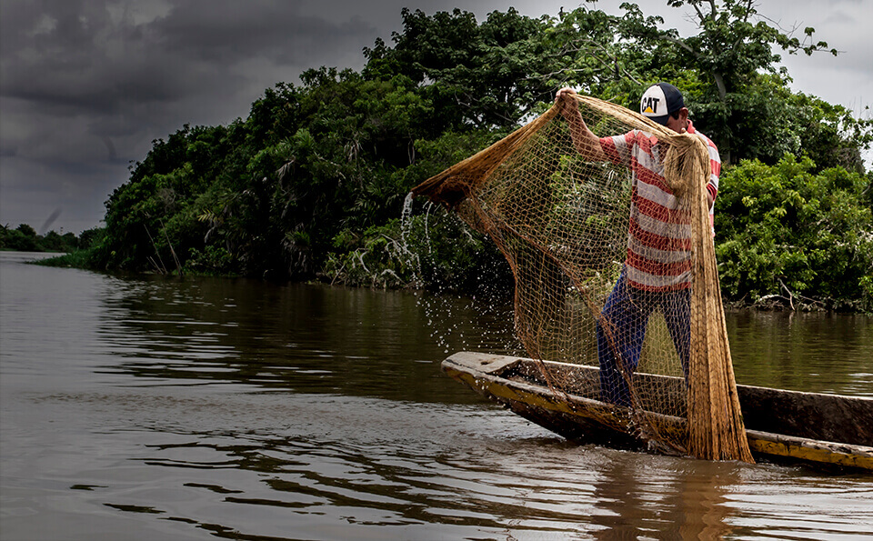 Pescador sostiene malla en una canoa sobre el mar