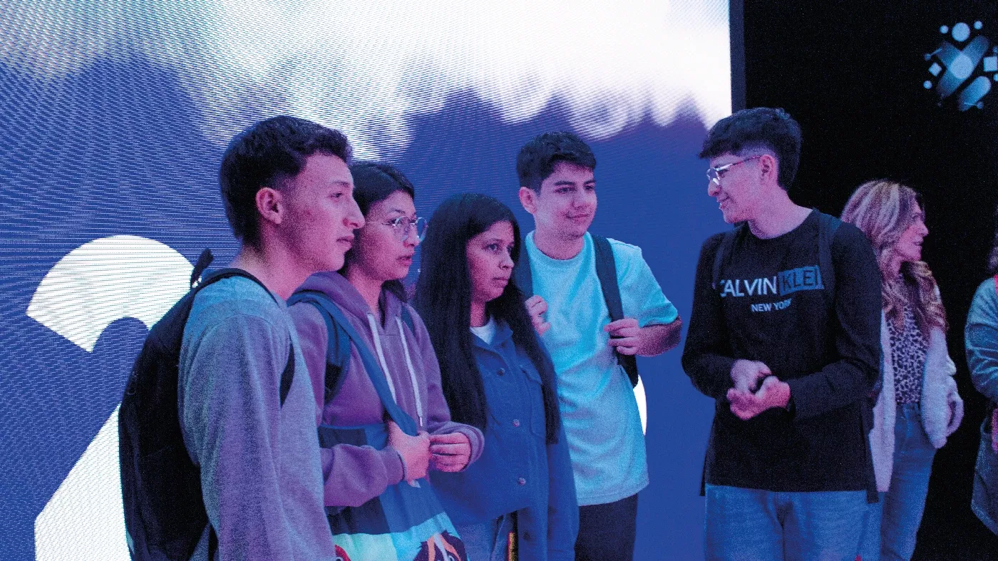 Grupo de estudiantes conversando con atención frente a una pantalla iluminada en un ambiente interactivo y tecnológico.