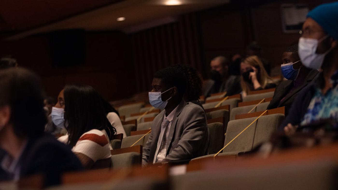 Hombres y mujeres sentados en un auditorio usando tapabocas.