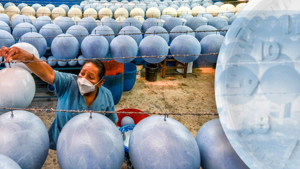 Una mujer arregla unos balones de fútbol, en una fábrica. A un lado un reloj.