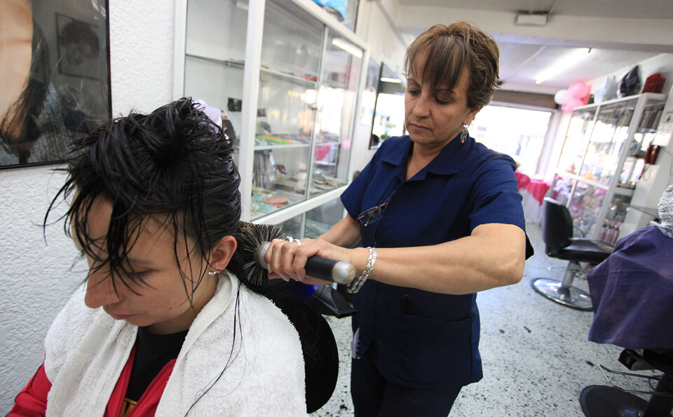 una peluquera con uniforme azul cepilla el pelo de una mujer