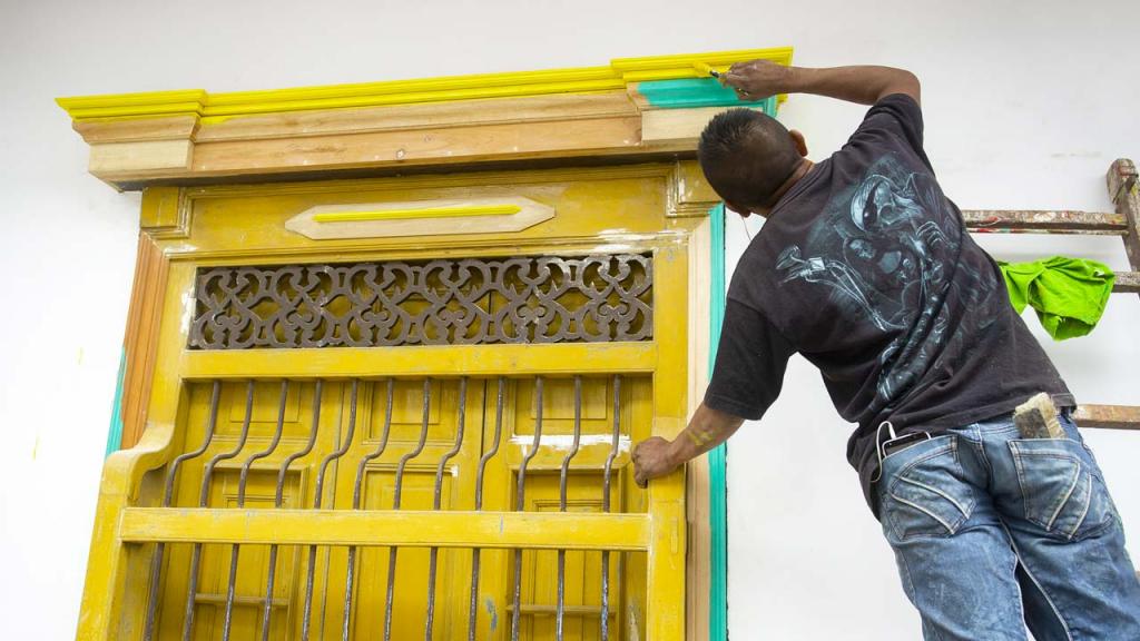 Hombre pinta una ventana de una casa de color amarillo. 